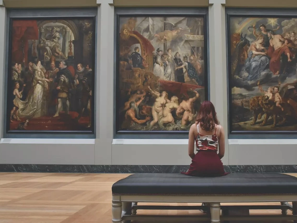 A woman sitting in an art gallery looking at the paintings. 