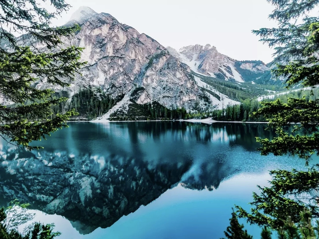 A beautiful lake surrounded by trees and snowy mountains. 
