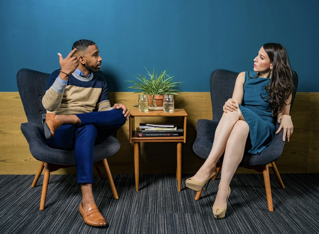 A man and a woman sitting on comfortable chairs, having a conversation.