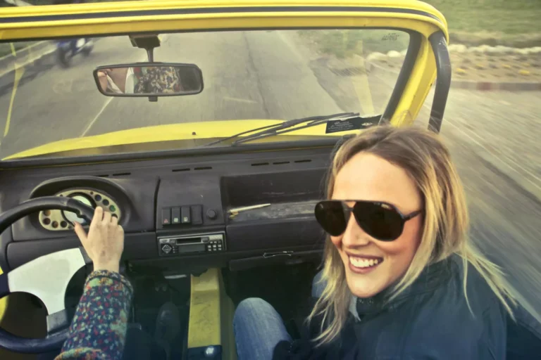 Two people driving in an open-topped car.